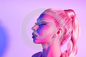 Fashion model woman with a bright make-up in colourful bright neon uv lights posing in studio