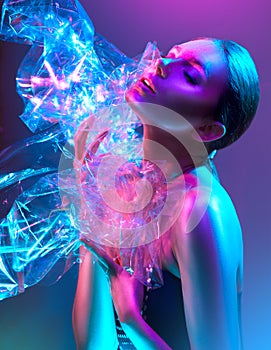Fashion model woman in colorful bright neon lights posing in studio through transparent film. Portrait of beautiful girl in UV