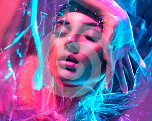 Fashion model woman in colorful bright neon lights posing in studio through transparent film. Portrait of beautiful girl in UV