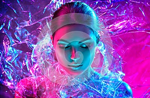 Fashion model woman in colorful bright neon lights posing in studio through transparent film. Portrait of beautiful sexy girl