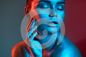 Fashion model woman in colorful bright sparkles and neon lights posing in studio, on black, portrait of beautiful sexy girl