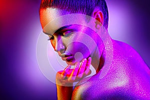 Fashion model woman in colorful bright sparkles and neon lights posing in studio, portrait of beautiful girl