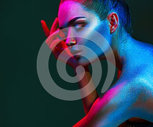 Fashion model woman in colorful bright sparkles and neon lights posing in studio, portrait of beautiful girl