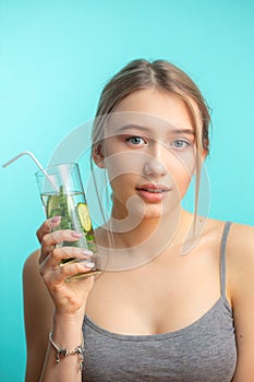 Spa woman with towel on head holding glass of cucumber water isoalted over blue photo