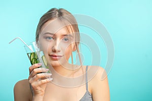 Spa woman with towel on head holding glass of cucumber water isoalted over blue photo