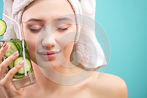 Spa woman with towel on head holding glass of cucumber water isoalted over blue photo