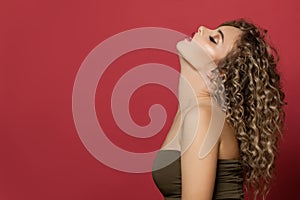 Fashion model woman with healthy curly hair on red background portrait. Pretty lady with trendy hair styling and hair dye