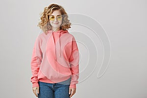 Fashion is in my blood. Good-looking caucasian girl with curly hair wearing trendy eyewear and pink hoodie, smiling and