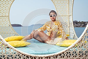 Fashion outdoor photo of beautiful girl posing on the wicker nest chair