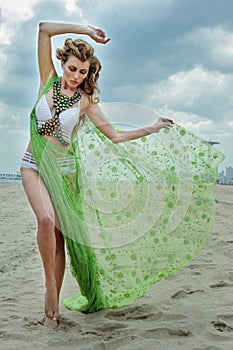 Fashion outdoor photo of beautiful woman with blond hair wearing luxury design bikini and holding fluttering cover up.
