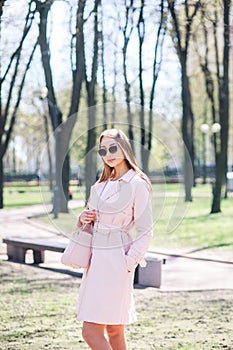 Fashion outdoor photo of beautiful young woman with blond hair in elegant clothes and sunglasses posing in sunny park