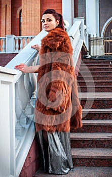 Fashion outdoor photo of glamour woman with dark hair wearing luxurious fur coat and leather gloves