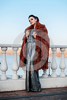 Fashion outdoor photo of glamour woman with dark hair wearing luxurious fur coat and leather gloves