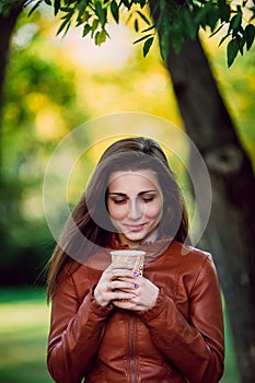 Fashion outdoor portrait of gorgeous smiling woman in brown leather jacket with cup of coffe. Fashionable girl in trendy clothes p