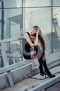 Fashion outdoor portrait of sexy beautiful woman with brown hair wearing in black dress, hose and high heels. Posing on creative