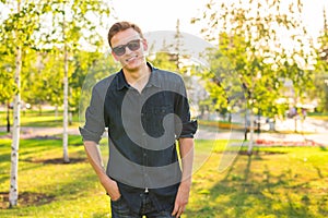 Fashion, people and lifestyle concept - Close-up portrait of happy cheerful confident handsome man in sunglasses in park