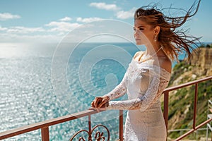 Fashion photo of a beautiful woman bride with light hair down in a luxurious wedding dress posing on a balcony overlooking the sea