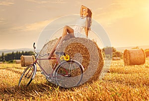 Fashion photo, beautiful woman sitting on a bale of wheat, next to the old bike