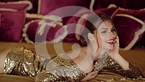 Fashion photo of a beautiful young woman in a pretty gold dress posing in bed. Portrait of beautiful young girl with