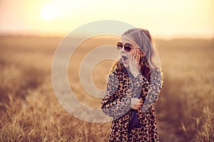 Fashion photo of a little girl in leopard print dress, sunglasses and straw hat at the evening wheat field