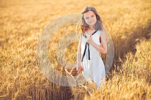 Fashion photo of a little girl in white dress and straw hat at the evening wheat field