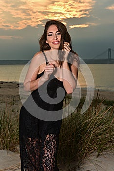 Fashion photo of glamour model in black lace dress posing pretty on the beach.