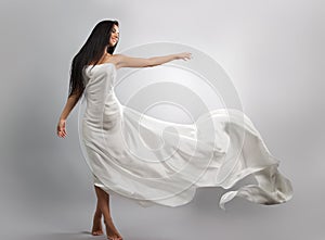 Fashion photo of young girl in white dress flying tissue. Lightweight material.