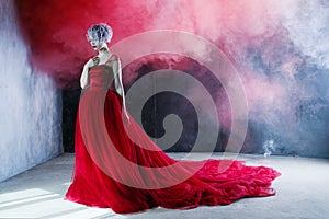 Fashion photo of young magnificent woman in red dress. Textured background, smoke
