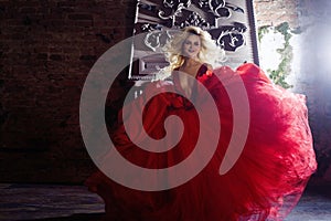 Fashion photo of young magnificent woman. Running towards camera. Seductive blonde in red dress with fluffy skirt