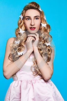 Fashion photo of young woman against blue background wearing pink dress and hair pins look like butterflies