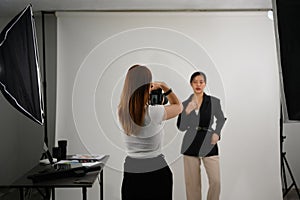 Fashion photographer taking picture of female model with digital camera in lighting studio