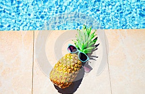 Fashion pineapple with sunglasses, blue water pool background, summer holidays,