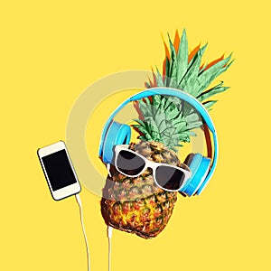 Fashion pineapple with sunglasses and headphones listens music on smartphone over yellow background