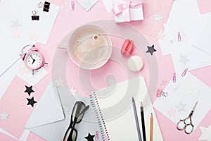 Fashion pink woman workplace background. Coffee, macaron, office supply, gift and clean notebook on pastel desk top view.