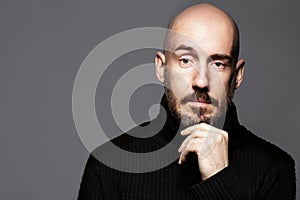 Fashion Portrait of a 40-year-old man standing over a light gray background in a black sweater. Close up. Classic style. Bald