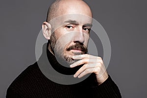 Fashion Portrait of a 40-year-old man standing over a light gray background in a black sweater. Close up. Classic style. Bald