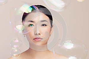 Fashion portrait of asian sweet and attractive young woman on background soap bubbles, fake eyelashes and make-up