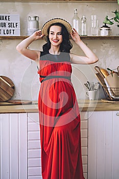 Fashion portrait of attractive stylish pregnant lady in long red sarafan and straw hat, photo of the happy and beautiful