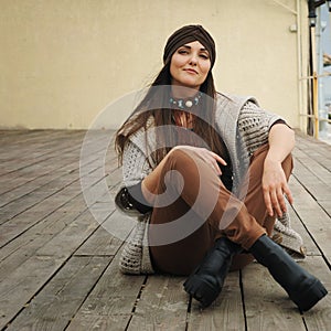 Fashion portrait of a beautiful smiling brunette woman sitting in front of town beach, smiling and looking at camera