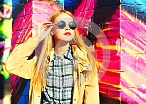 Fashion portrait of beautiful stylish blonde young woman on city street over colorful graffiti background