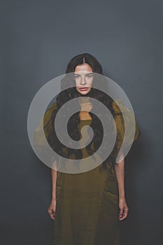 Fashion portrait of beautiful woman with long curly hair in green tulle dress posing on black background