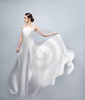 Fashion portrait of a beautiful woman in a waving white dress. Light fabric flies in the wind