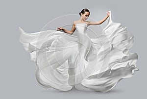 Fashion portrait of a beautiful woman in a waving white dress. Light fabric flies in the wind