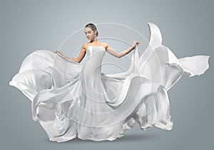 Fashion portrait of a beautiful woman in a waving white dress. Light fabric flies in the wind