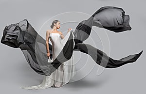 Fashion portrait of a beautiful woman in a white and black dress. The fabric flies in the wind