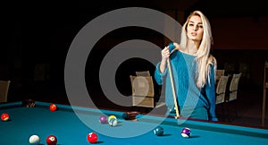 Fashion portrait of beautiful young blonde girl plays billiard