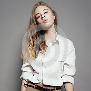 Fashion portrait of a beautiful young blonde woman in a white shirt in the studio on a gray background