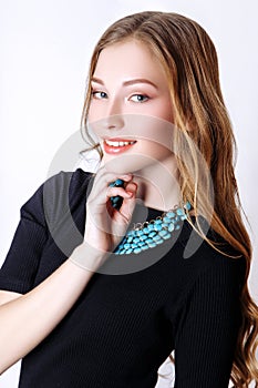 Fashion portrait of beautiful young woman with blond hair. Girl in a black dress and blue necklace on a white background