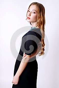 Fashion portrait of beautiful young woman with blond hair. Girl in a black dress and blue necklace on a white background