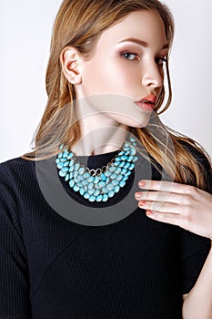 Fashion portrait of beautiful young woman with blond hair. Girl in a black dress and blue necklace on a white background